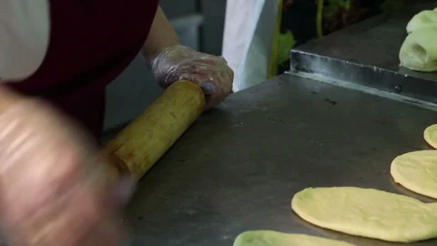 A bakery worker uses her hands and a rolling pin to roll out dough on a kitc Stock Footage 320308024