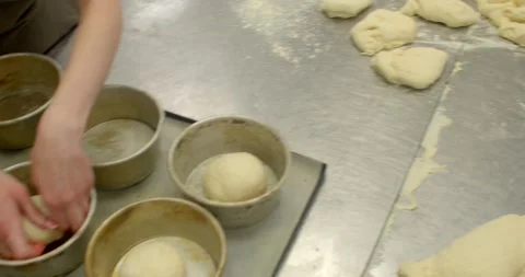 Bakery workstation with hands placing dough into metal molds on floured, with Stock Footage 344597067
