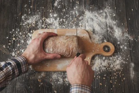 Baking and cooking concept background. Hands of baker closeup cutting bread loaf Foto stock