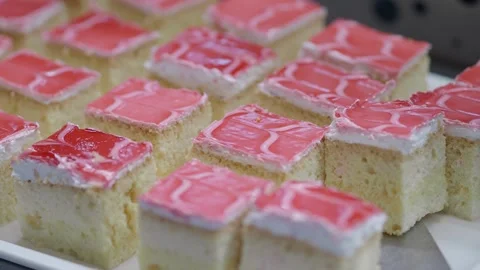 Baking and decorating pink frosted cake squares at a local bakery Stock Footage 345188210