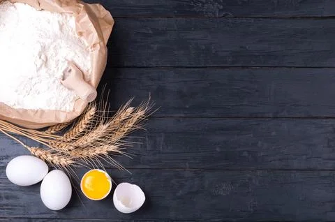 Baking background. Flour in paper bag, wheat and eggs on dark wooden table... Stock Photos