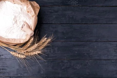 Baking background. Flour in paper bag and wheat on dark wooden table. Ingre.. Stock Photos
