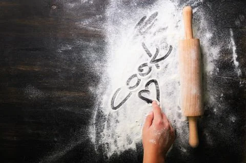 Baking background. Heart of flour, text Cook and rolling pin on dark table with Stock Photos