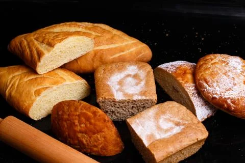 Baking on a black background with a rolling pin. Lots of pastries and bread. Stock Photos