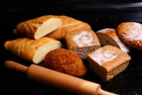 Baking on a black background with a rolling pin. Lots of pastries and bread. Stock Photos