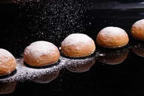 Baking on a black background. White buns sprinkled with powder and flour. Stock Photos