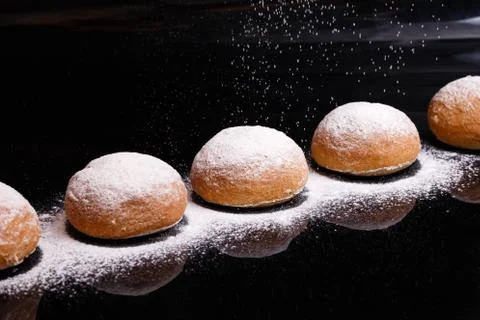 Baking on a black background. White buns sprinkled with powder and flour. Stock Photos