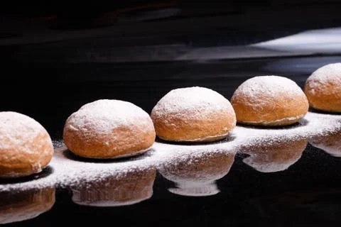 Baking on a black background. White buns sprinkled with powder and flour. Stock Photos