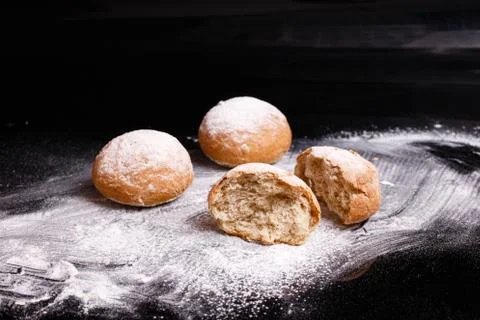 Baking on a black background. White buns sprinkled with powder and flour. Stock Photos