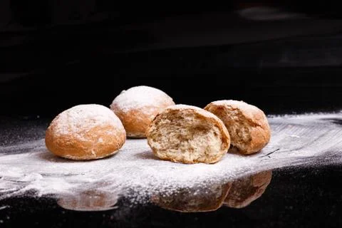 Baking on a black background. White buns sprinkled with powder and flour. Stock Photos