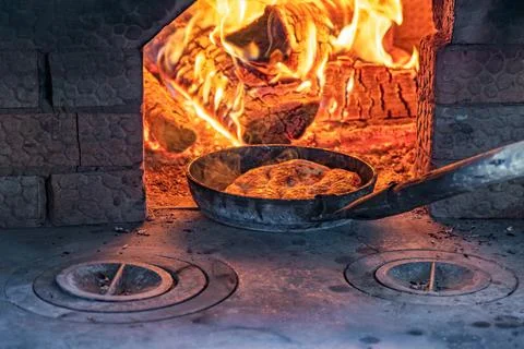 Baking bread in a rustic brick oven with firewood and glowing flames Stock Photos