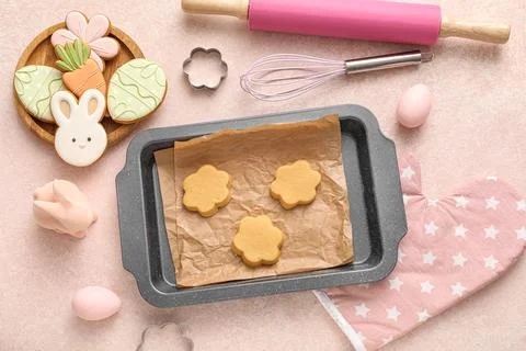 Baking dish with raw Easter cookies, eggs and kitchen utensils on pink grunge Stock Photos