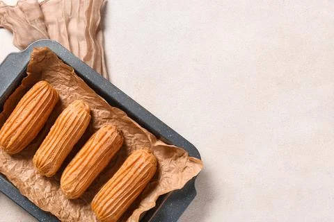 Baking dish with tasty eclairs on light grunge background Stock Photos