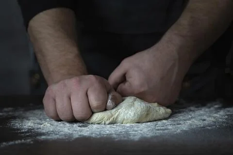 Baking fresh bread in the bakery, hands of male knead dough on kitchen table Stock Photos