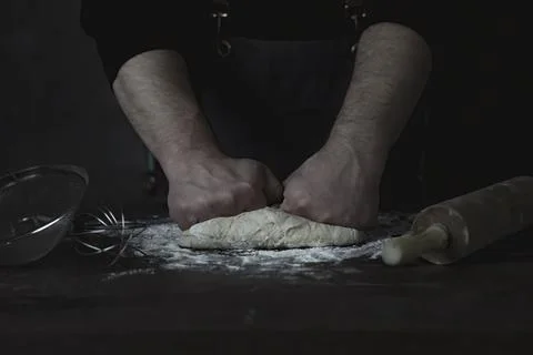 Baking fresh bread in the bakery, hands of male knead dough on kitchen table Stock Photos