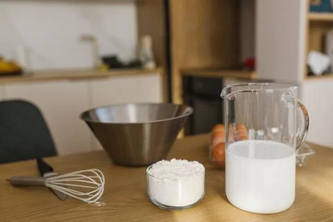 Baking ingredients on kitchen table with milk flour eggs and whisk, home cooking Stock Photos