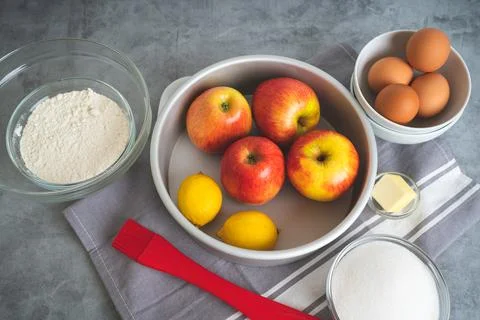 Baking pan, apples, lemons, eggs, sugar, and flour in bowls close-up on a k.. Stock Photos