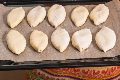 On a baking sheet are raw Russian dough pies with filling. Homemade baking Stock Photos