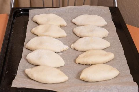 On a baking sheet are raw Russian dough pies with filling. Homemade baking Stock Photos
