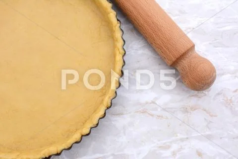 Baking tin lined with pastry, wooden rolling pin beside Stock Photos