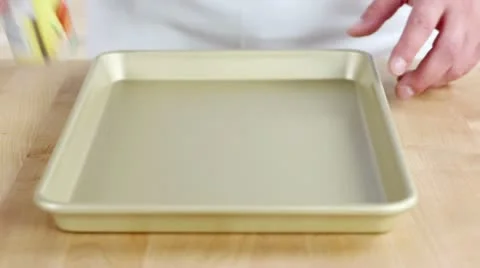 A baking tray being sprayed with a non-stick spay and dusted with flour Stock Footage 24673057