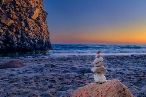Balance stone stack and big natural rock on sandy beach at sunset. Stock Photos