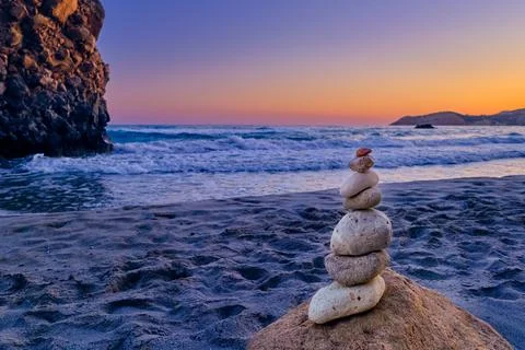 Balance stone stack and big natural rock on sandy beach at sunset. Stock Photos