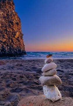 Balance stone stack and big natural rock on sandy beach at sunset. Stock Photos