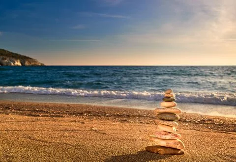 Balance stone stack on sandy beach in sunset sunlight, sea waves. Cairn lit by Stock Photos