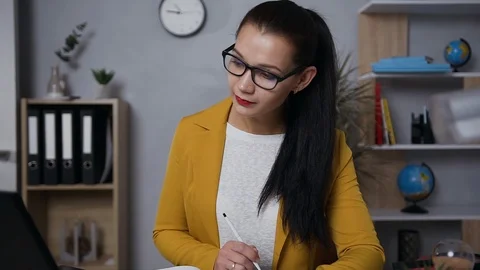 Balanced good-looking modern brunette businesswoman in glasses making notes on Stock Footage 124702306