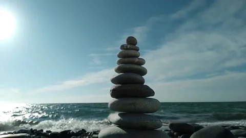 Balanced pebble pyramid swing in the wind on the beach Stock Footage 163665706
