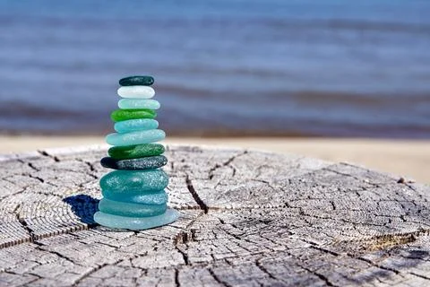 A balanced pyramid of multi-colored glass pebbles on a wooden stump against.. Stock Photos