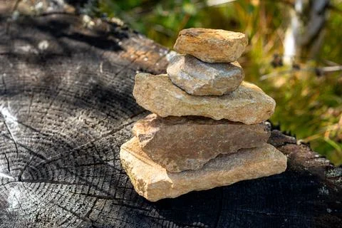 Balanced stack of natural stones placed on cut tree stump in forest. Stock Photos