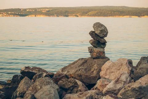 Balanced stack of stones on a rocky shore overlooking calm sea and a distan.. Stock Photos