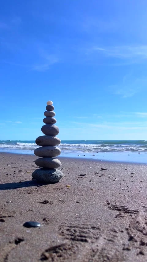 Balanced Stone Stack on Peaceful Beach with Gentle Waves and Blue Sky Stock Footage 310210585