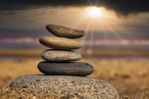 Balanced stone stack at sunset on a serene beach with soft waves lapping the Stock Photos