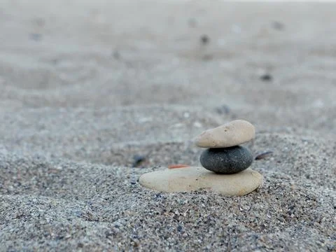 Balanced stones rest on sandy beach during daylight near ocean water in a 스톡 사진