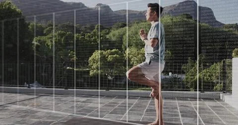 Balancing man holding tree pose wearing fitness tracker on terrace with grid  Stock Photos