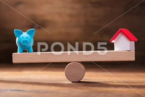 Balancing Of Piggybank And House Model On The Wooden Seesaw Stock-Fotos