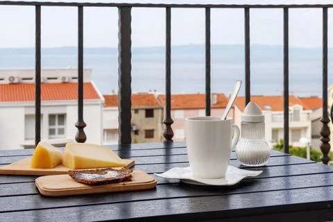 Balcony breakfast with coffee cup, bread with butter, cheese, and a soft Ad.. Stock Photos