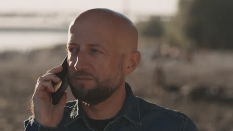 Bald and handsome man with a stylish beard is standing on the beach during a Stock Footage 145873094