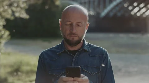 Bald and handsome manager with a stylish beard is standing in the park and is Stock Footage 135076112