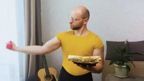 Bald athletic man trains biceps dumbbells and looks at a plate of food Stock Footage 243758768