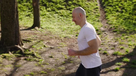 A bald athletic man is working out in the park. The athlete, dressed in a white Stock Footage 279020629
