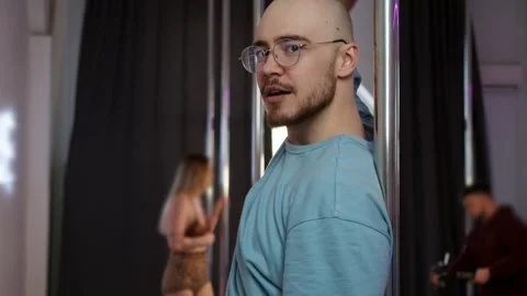A bald, bearded and stern man is pole-dancing and seductively looking directly Stock Footage 305323879