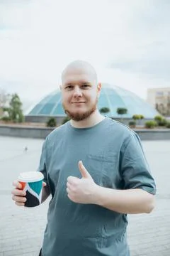 Bald bearded man drinking coffee outdoors thumb up Stock Photos
