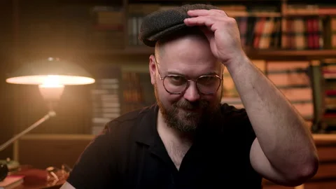 Bald bearded man looks at camera, puts on glasses and silk retro eight-piece cap Stock Footage 260948406
