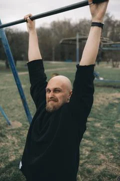 A bald bearded man tries to pull himself up on a horizontal bar Stock Photos