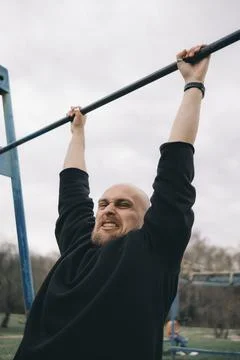 A bald bearded man tries to pull himself up on a horizontal bar Stock Photos