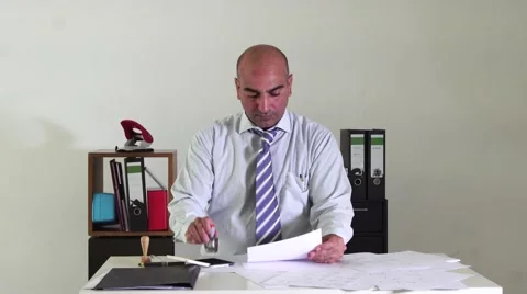 Bald bureaucrat sitting at desk in office stamping paperworks Stock Footage